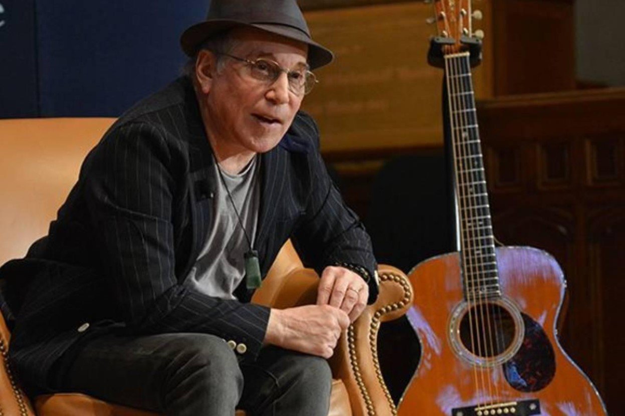 Paul Simon in Hat and Glasses Sitting Next to Guitar