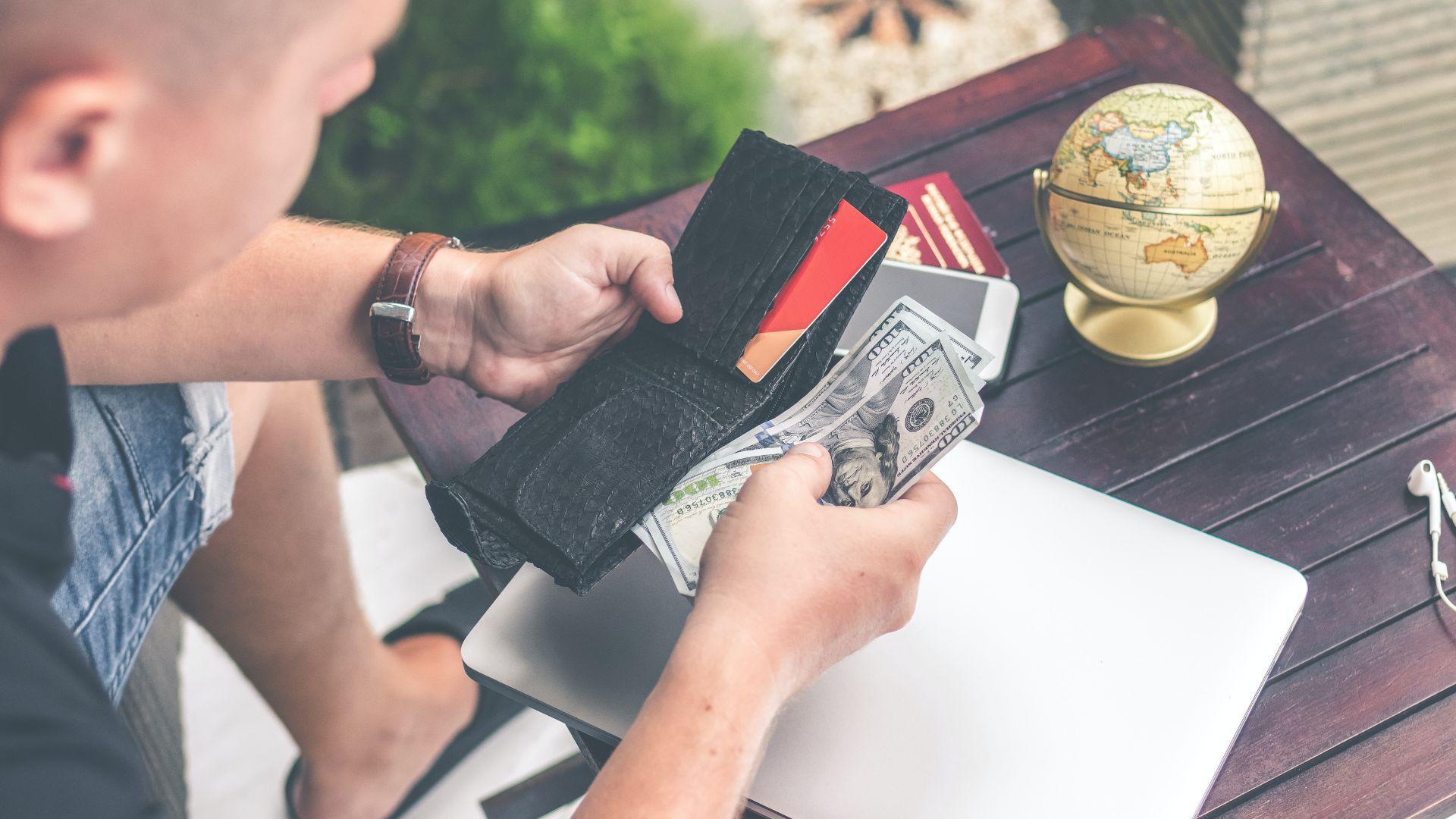 A man pulling money out of a wallet while sitting at a table