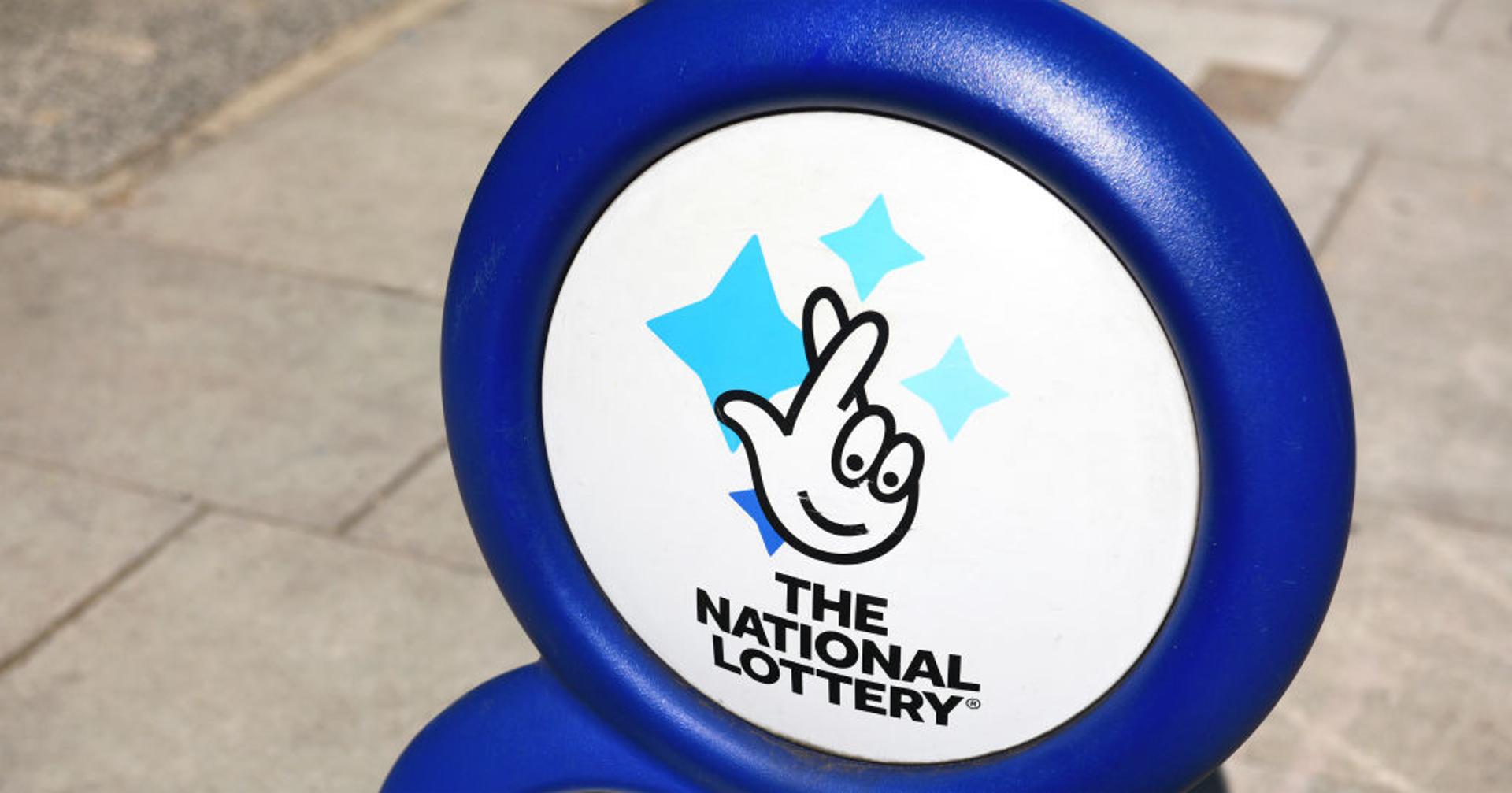 Plastic sign of the United Kingdom national lottery sits outside of a small shop