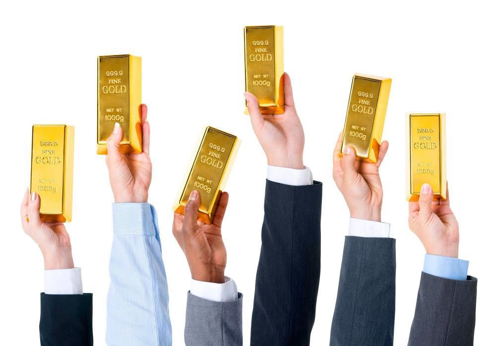 Six Hands Holding Up Gold Bars in Front of White Background