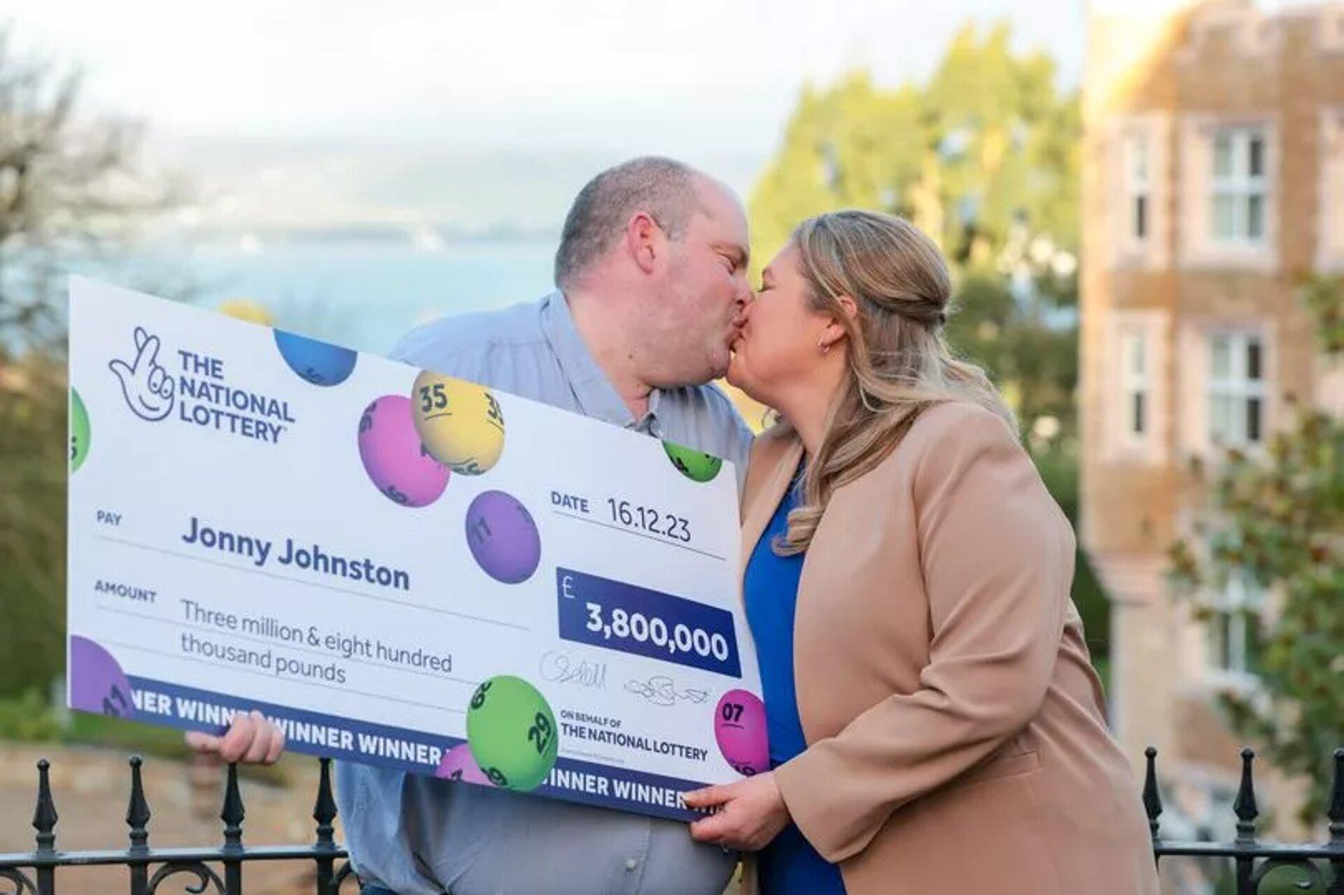 Jonny Johnson and his wife, Christina Willaims, share a kiss as they hold the Lottery cheque
