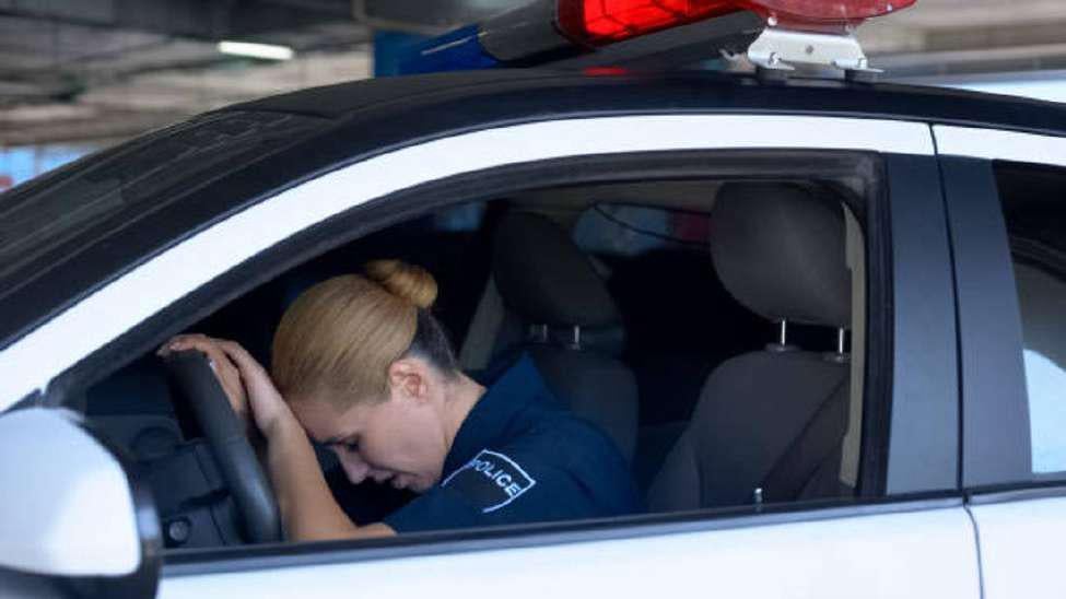 Female police officer rests her head on the steering wheel in her squad car out of exhaustion