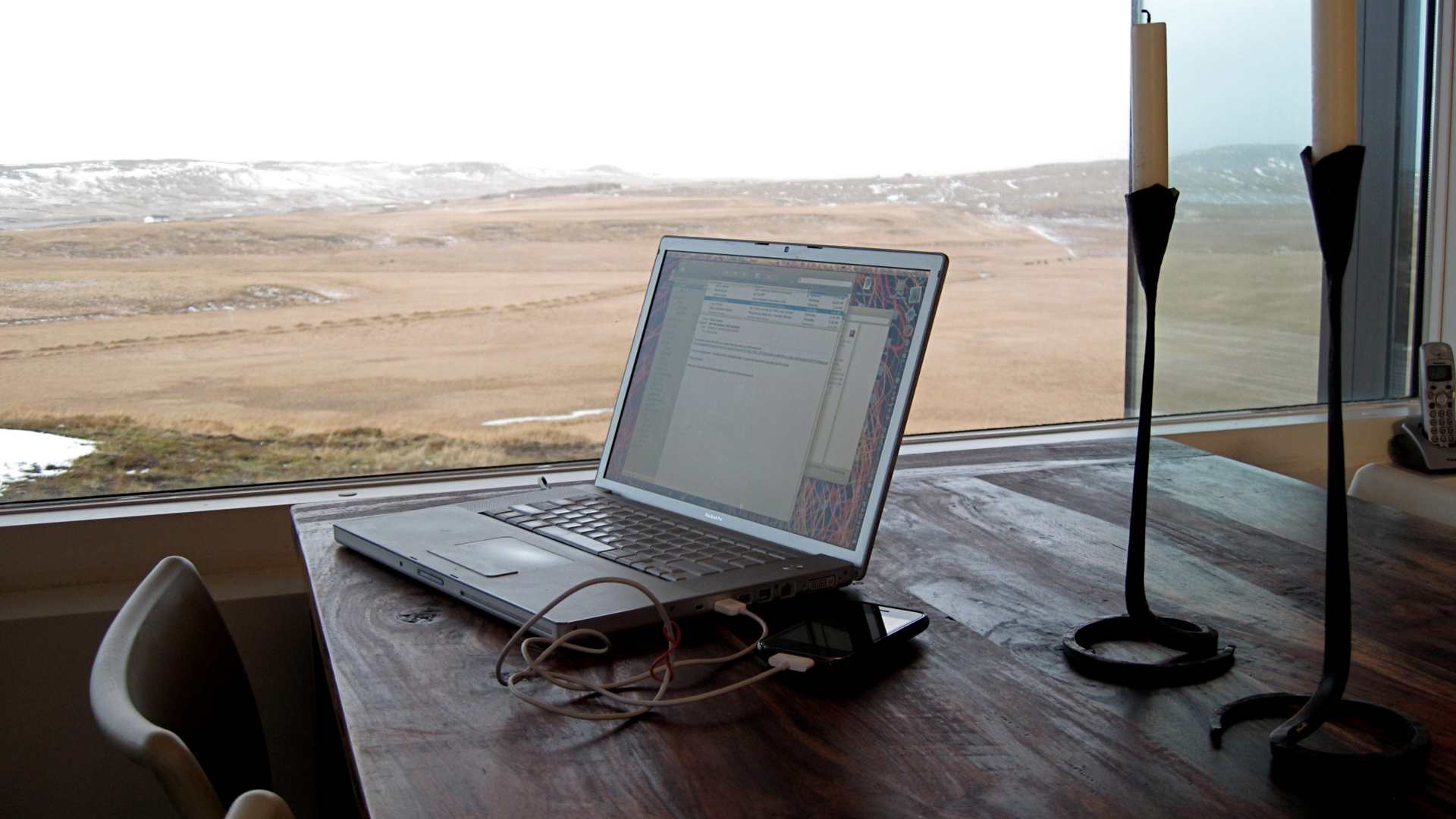 A laptop in front of a window with a beautiful view, surrounded by two unlit candles.