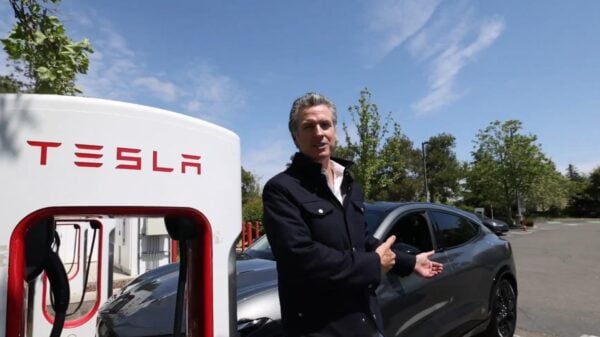 California Governor Gavin Newsom stands next to a Tesla charger with his own electric vehicle